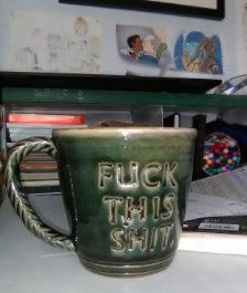 A forest green, glazed clay mug with a handle like braided rope. Stamped into the front are the words FUCK THIS SHIT.